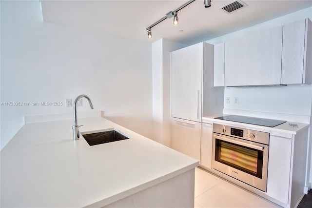 kitchen with sink, light tile patterned floors, black electric cooktop, oven, and white cabinets