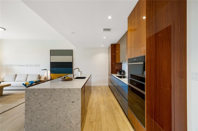 kitchen featuring light stone countertops, a kitchen island with sink, sink, and light hardwood / wood-style flooring