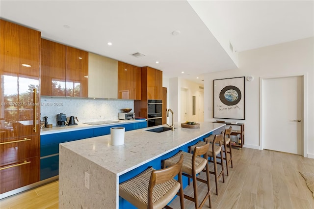 kitchen featuring an island with sink, light stone counters, a kitchen bar, and light hardwood / wood-style flooring