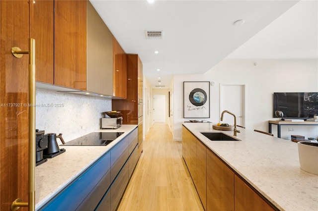 kitchen with sink, light stone counters, tasteful backsplash, light wood-type flooring, and black electric stovetop