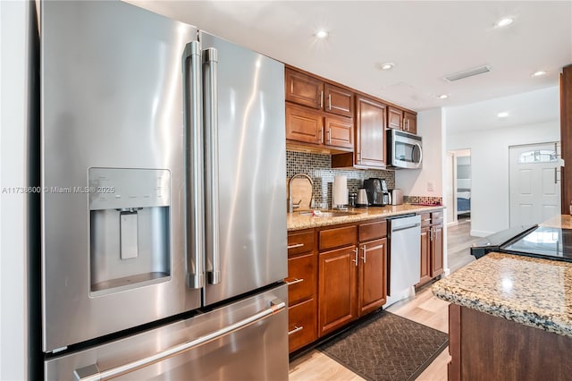 kitchen with light stone counters, sink, light wood-type flooring, and appliances with stainless steel finishes