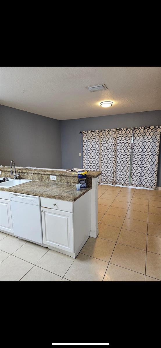 kitchen featuring sink, a textured ceiling, light tile patterned floors, white dishwasher, and white cabinets