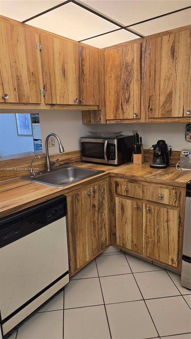 kitchen featuring white dishwasher, butcher block counters, sink, and light tile patterned floors