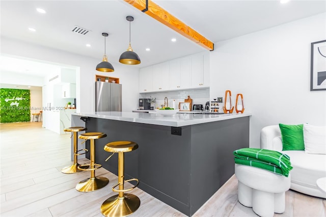 kitchen featuring white cabinetry, stainless steel refrigerator, a kitchen breakfast bar, pendant lighting, and backsplash