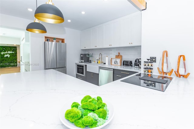 kitchen featuring pendant lighting, appliances with stainless steel finishes, white cabinetry, backsplash, and light stone counters