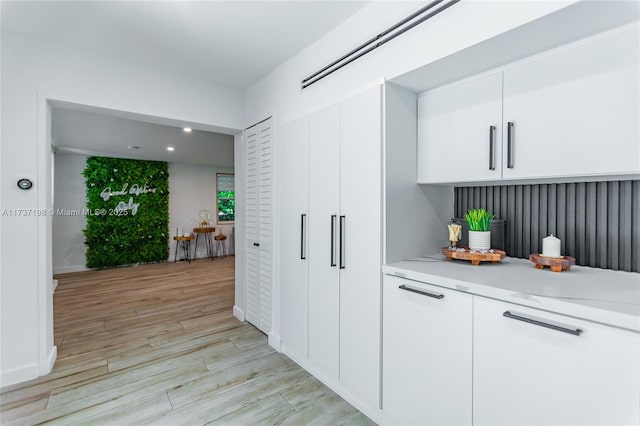 bar with white cabinetry, light stone counters, and light hardwood / wood-style floors