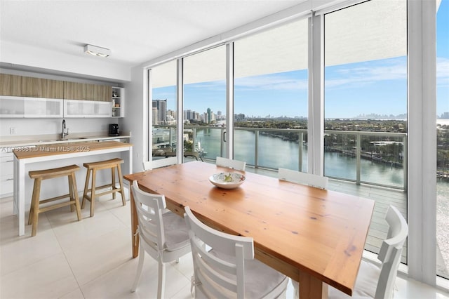 dining area featuring floor to ceiling windows, a water view, sink, and light tile patterned flooring