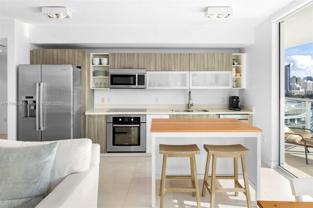 kitchen featuring a breakfast bar, sink, light tile patterned floors, expansive windows, and stainless steel appliances