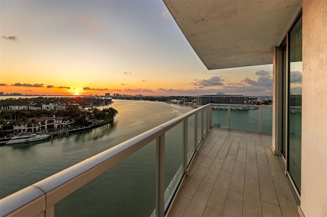 balcony at dusk featuring a water view