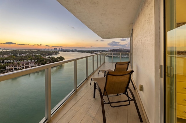 balcony at dusk featuring a water view