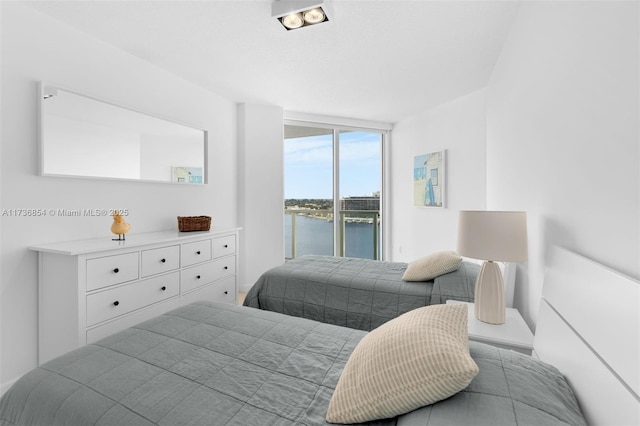 bedroom with floor to ceiling windows, a water view, and access to exterior