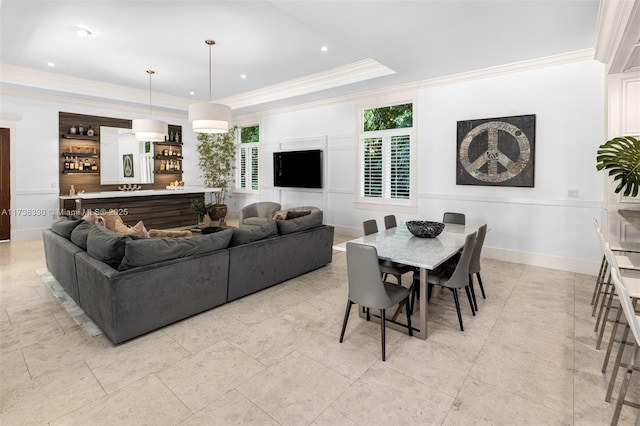 dining space with a tray ceiling, ornamental molding, and bar area