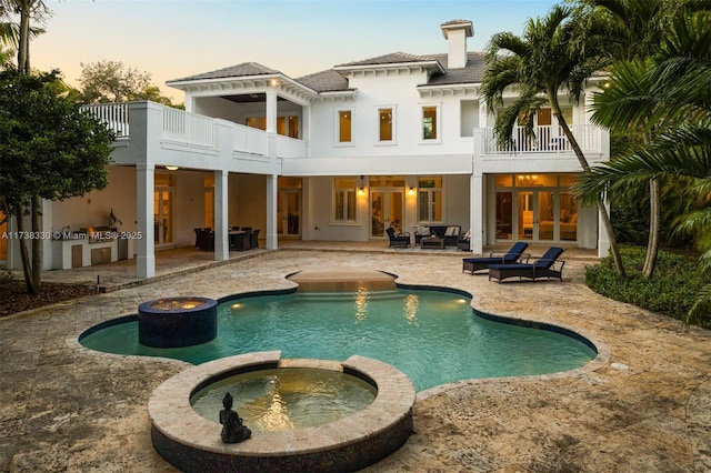 back house at dusk with area for grilling, a patio area, outdoor lounge area, and a balcony