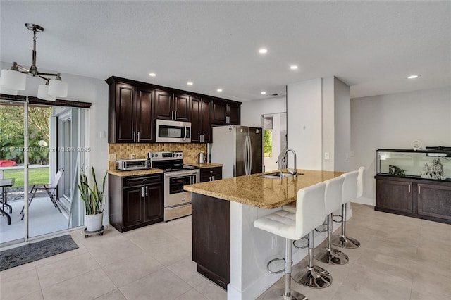 kitchen featuring sink, tasteful backsplash, light stone counters, appliances with stainless steel finishes, and an island with sink