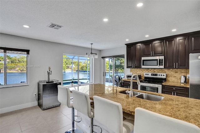 kitchen featuring sink, appliances with stainless steel finishes, tasteful backsplash, light stone countertops, and decorative light fixtures