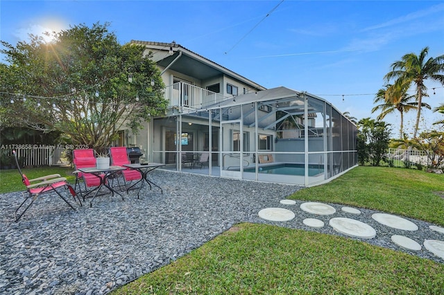 back of property featuring a balcony, glass enclosure, a lawn, a fenced in pool, and a patio