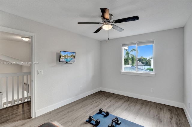 exercise area with ceiling fan, a textured ceiling, and light wood-type flooring