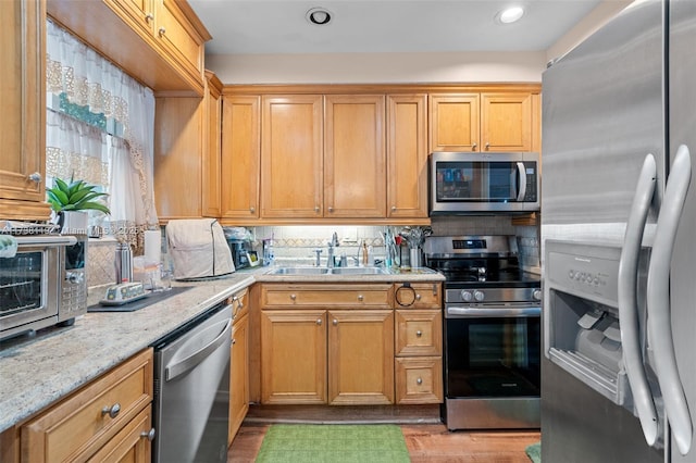 kitchen with sink, light stone counters, tasteful backsplash, light wood-type flooring, and stainless steel appliances