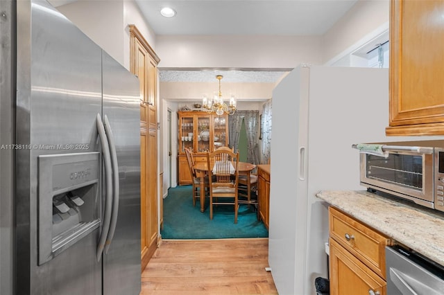 kitchen featuring an inviting chandelier, decorative light fixtures, light hardwood / wood-style flooring, appliances with stainless steel finishes, and light stone countertops