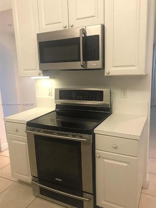 kitchen with appliances with stainless steel finishes, light tile patterned floors, and white cabinets