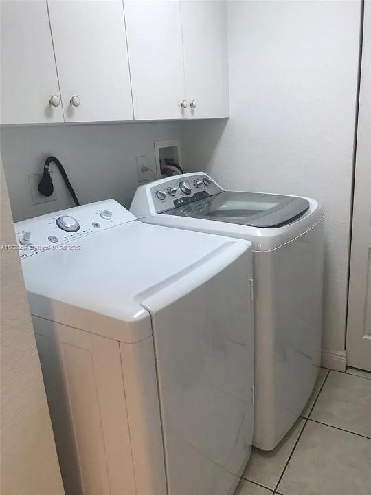 laundry room featuring washing machine and dryer, cabinets, and light tile patterned flooring