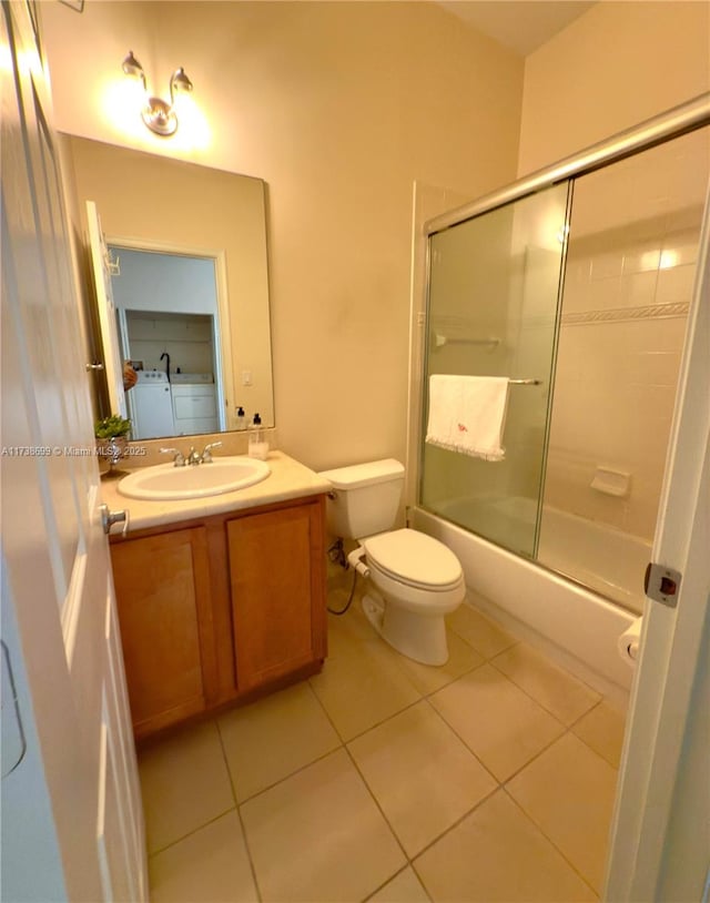 full bathroom featuring shower / bath combination with glass door, washer / clothes dryer, toilet, vanity, and tile patterned flooring