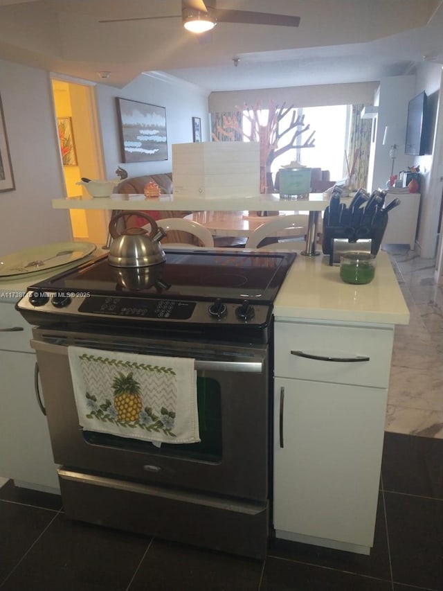 kitchen with stainless steel range with electric stovetop, dark tile patterned flooring, and white cabinetry