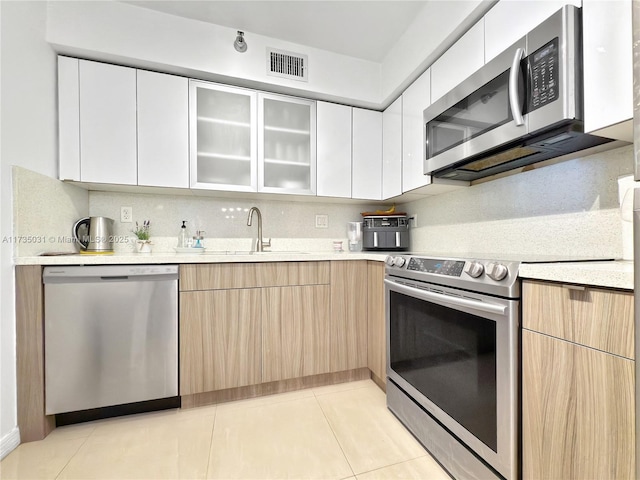 kitchen featuring sink, light tile patterned floors, white cabinetry, stainless steel appliances, and decorative backsplash