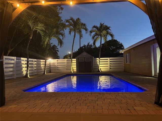 pool at dusk with a storage shed and a patio area