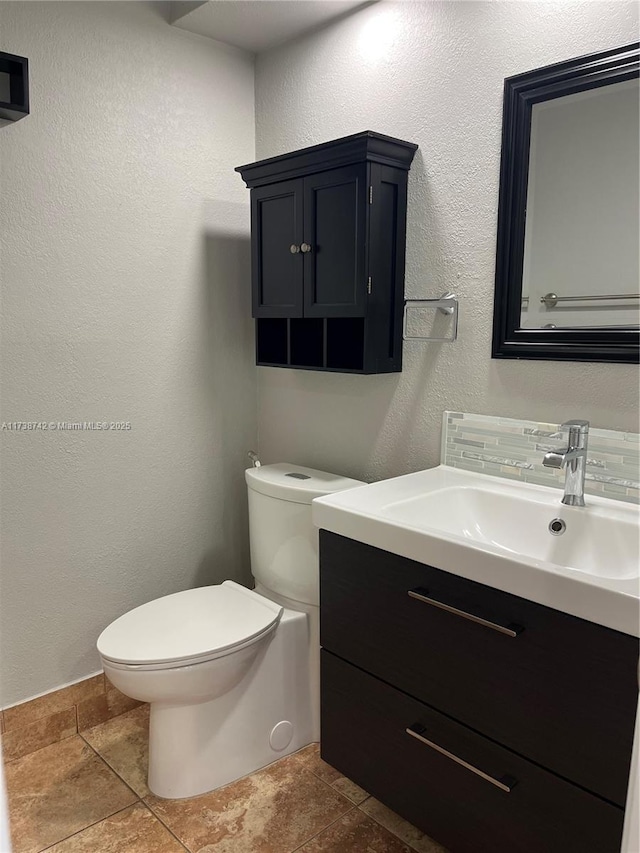 bathroom with toilet, vanity, and decorative backsplash