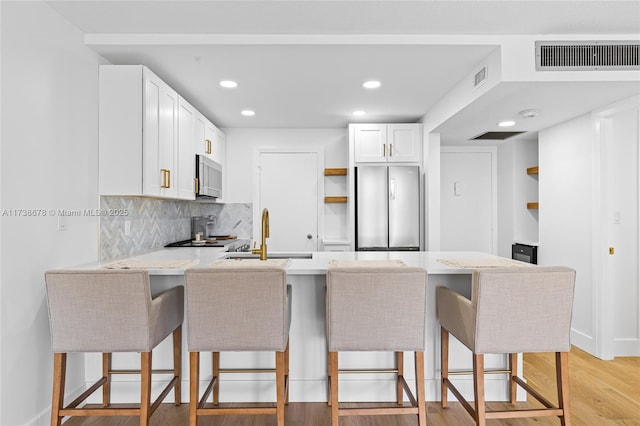 kitchen featuring a breakfast bar, stainless steel refrigerator, white cabinets, kitchen peninsula, and light hardwood / wood-style flooring