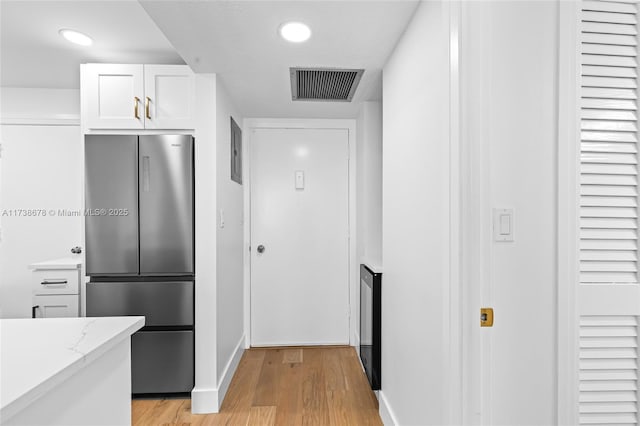 kitchen with white cabinetry, light stone countertops, light wood-type flooring, and stainless steel refrigerator