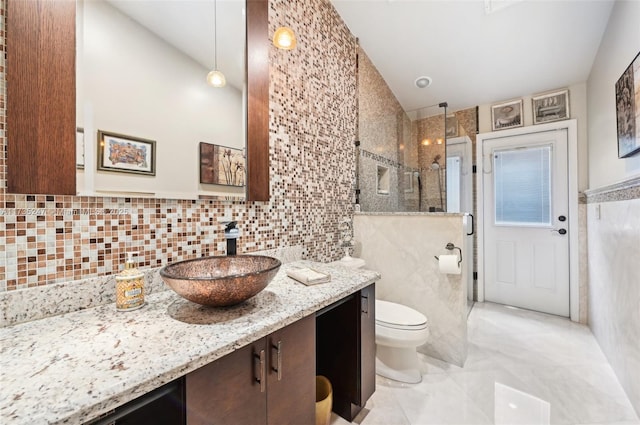 bathroom with a tile shower, tile walls, vanity, and toilet