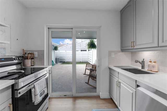 kitchen with appliances with stainless steel finishes, sink, gray cabinetry, decorative backsplash, and light wood-type flooring