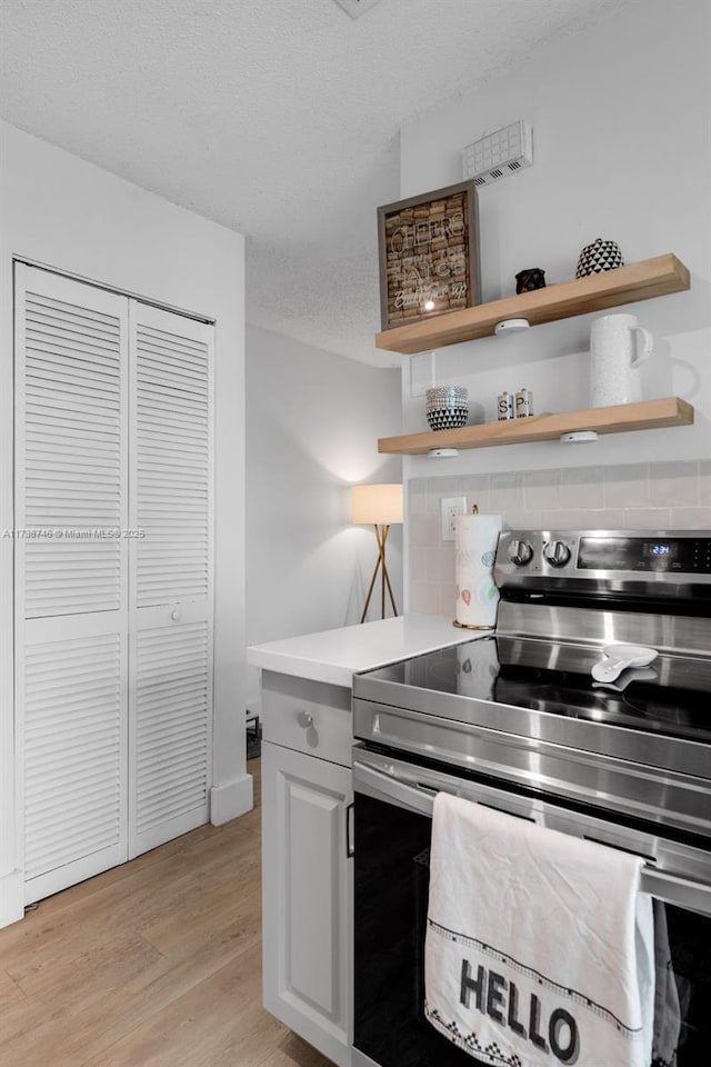 kitchen with electric stove, light hardwood / wood-style flooring, a textured ceiling, white cabinets, and decorative backsplash