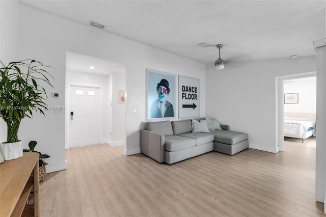 living room featuring ceiling fan, light hardwood / wood-style floors, and a textured ceiling