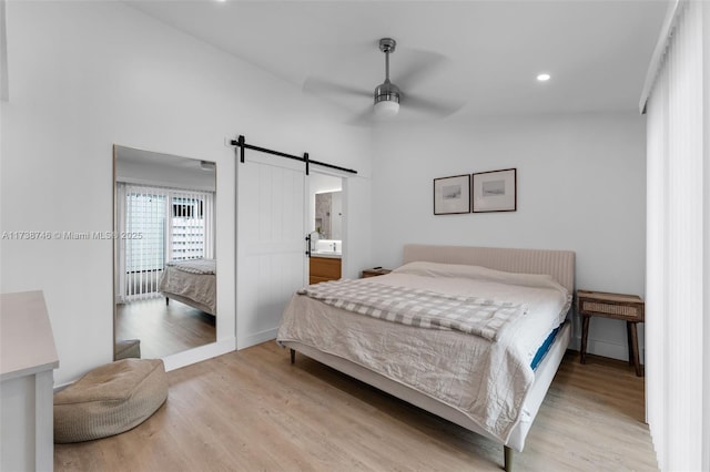 bedroom with ceiling fan, a barn door, and light wood-type flooring