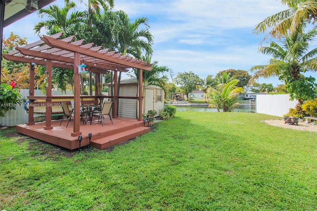 view of yard with a deck with water view, a pergola, and a storage unit