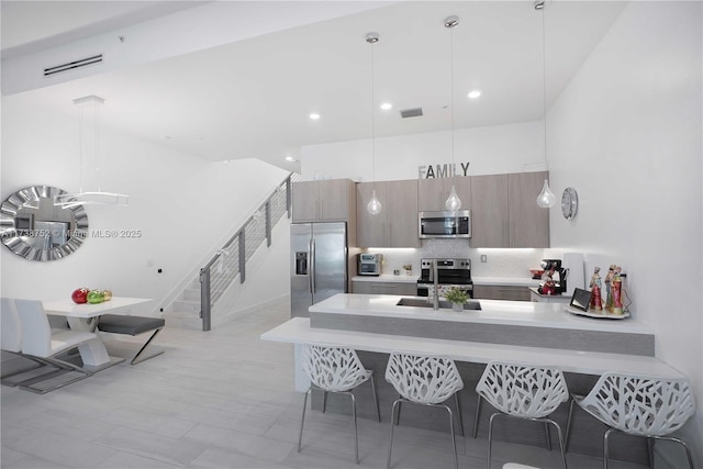 kitchen featuring sink, hanging light fixtures, a towering ceiling, stainless steel appliances, and tasteful backsplash