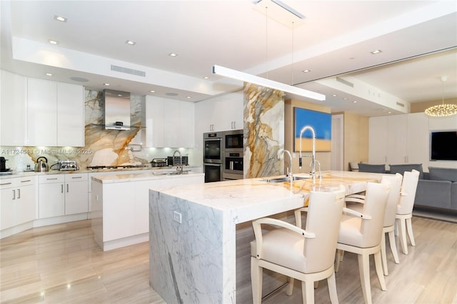 kitchen with a breakfast bar, a center island with sink, white cabinets, and decorative light fixtures