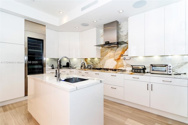 kitchen with white cabinetry, sink, a center island with sink, and wall chimney exhaust hood