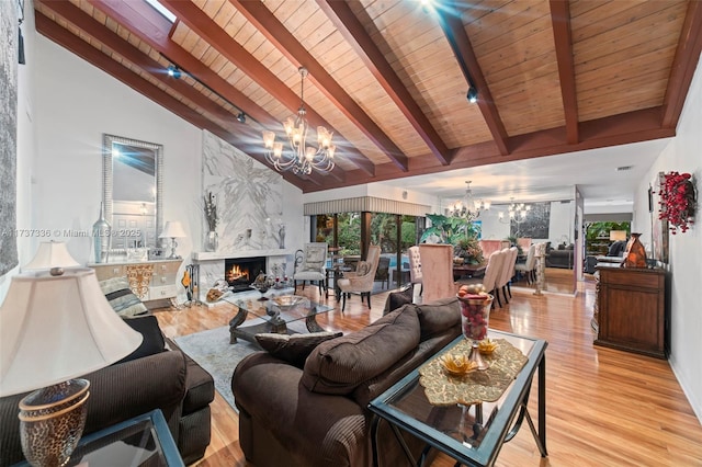 living room with beamed ceiling, a high end fireplace, light hardwood / wood-style floors, and a notable chandelier