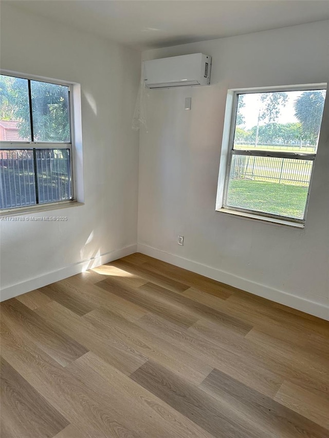 spare room featuring a healthy amount of sunlight, a wall mounted AC, and light hardwood / wood-style floors