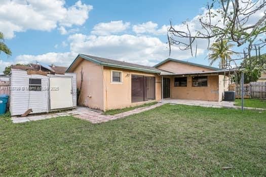 rear view of house featuring cooling unit, a gate, fence, and a lawn