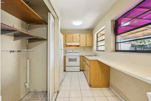 kitchen with light tile patterned floors, light countertops, white electric range, under cabinet range hood, and a sink