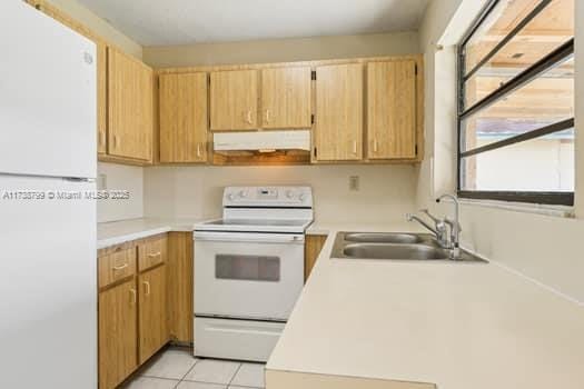 kitchen with light tile patterned flooring, under cabinet range hood, white appliances, a sink, and light countertops