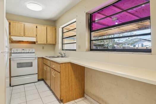 kitchen featuring light tile patterned flooring, under cabinet range hood, a sink, light countertops, and white electric range oven