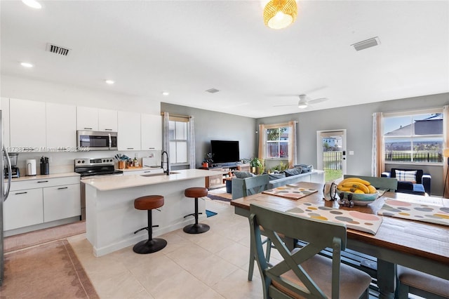 kitchen with sink, a breakfast bar area, white cabinetry, a center island with sink, and stainless steel appliances