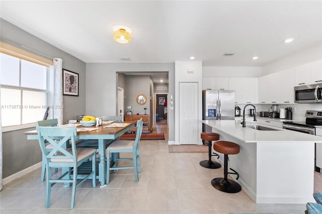 kitchen with sink, light tile patterned floors, appliances with stainless steel finishes, a kitchen island with sink, and white cabinetry