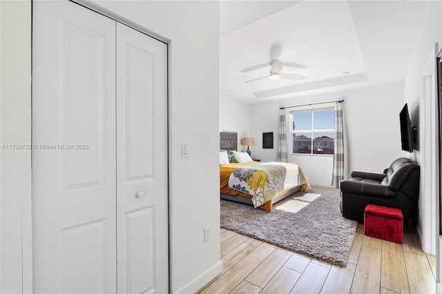 bedroom featuring ceiling fan, light wood-type flooring, and a tray ceiling